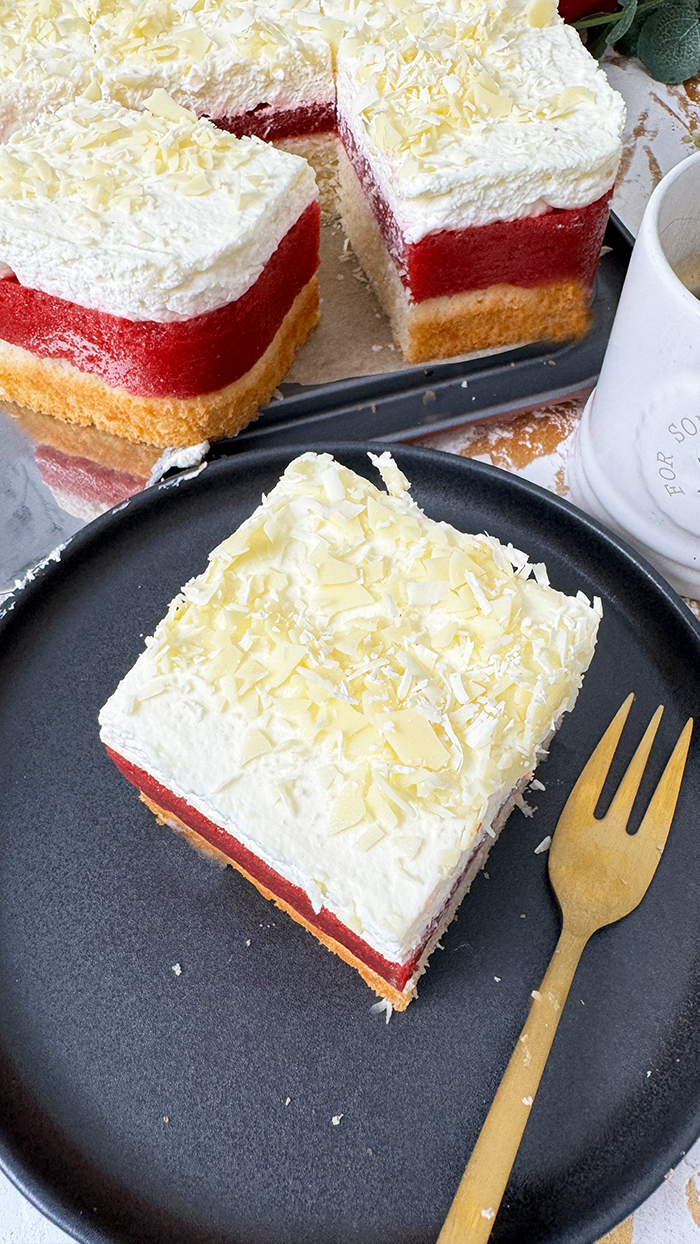 Das auf dem Bild gezeigte Kuchen ist ein "Frau Holle Kuchen". Er besteht aus mehreren Schichten: einem Biskuitboden, einer Erdbeer- oder Beerenschicht und einer cremigen oberen Schicht, die möglicherweise mit weißen Schokoladenraspeln garniert ist. Dieser Kuchen ist oft nach der Märchenfigur "Frau Holle" benannt und wird typischerweise mit frischen Zutaten zubereitet, wodurch eine köstliche Kombination aus Fruchtigkeit und Cremigkeit entsteht. 