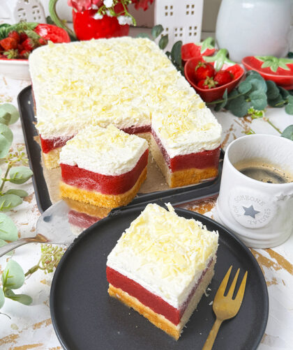 Das auf dem Bild gezeigte Kuchen ist ein "Frau Holle Kuchen". Er besteht aus mehreren Schichten: einem Biskuitboden, einer Erdbeer- oder Beerenschicht und einer cremigen oberen Schicht, die möglicherweise mit weißen Schokoladenraspeln garniert ist. Dieser Kuchen ist oft nach der Märchenfigur "Frau Holle" benannt und wird typischerweise mit frischen Zutaten zubereitet, wodurch eine köstliche Kombination aus Fruchtigkeit und Cremigkeit entsteht.