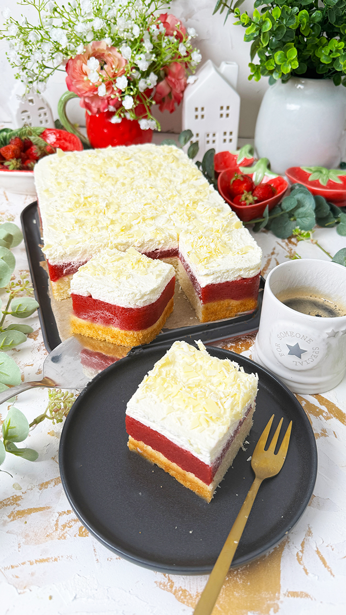 Das auf dem Bild gezeigte Kuchen ist ein "Frau Holle Kuchen". Er besteht aus mehreren Schichten: einem Biskuitboden, einer Erdbeer- oder Beerenschicht und einer cremigen oberen Schicht, die möglicherweise mit weißen Schokoladenraspeln garniert ist. Dieser Kuchen ist oft nach der Märchenfigur "Frau Holle" benannt und wird typischerweise mit frischen Zutaten zubereitet, wodurch eine köstliche Kombination aus Fruchtigkeit und Cremigkeit entsteht.