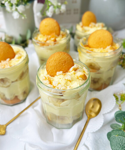 Das Bild zeigt mehrere Gläser, die mit dem berühmten Banana Pudding der Magnolia Bakery gefüllt sind. Jedes Glas ist in Schichten aufgebaut und enthält Vanillewaffeln, Bananenscheiben und cremigen Vanillepudding.