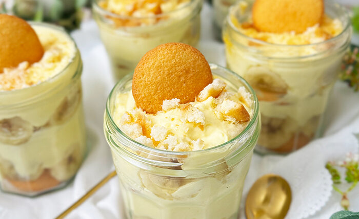 Das Bild zeigt mehrere Gläser, die mit dem berühmten Banana Pudding der Magnolia Bakery gefüllt sind. Jedes Glas ist in Schichten aufgebaut und enthält Vanillewaffeln, Bananenscheiben und cremigen Vanillepudding.