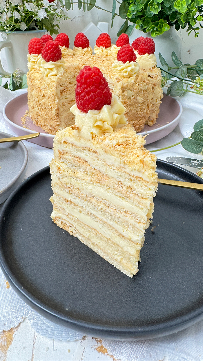 Eine Napoleon-Torte mit mehreren dünnen Schichten, die mit einer cremigen Füllung gefüllt sind und mit frischen Himbeeren dekoriert wurden