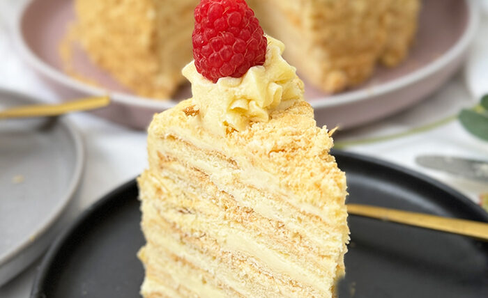 Eine Napoleon-Torte mit mehreren dünnen Schichten, die mit einer cremigen Füllung gefüllt sind und mit frischen Himbeeren dekoriert wurden