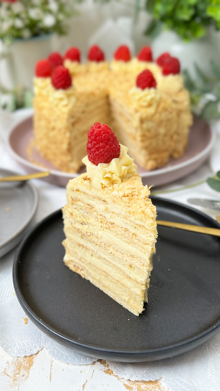 Eine Napoleon-Torte mit mehreren dünnen Schichten, die mit einer cremigen Füllung gefüllt sind und mit frischen Himbeeren dekoriert wurden