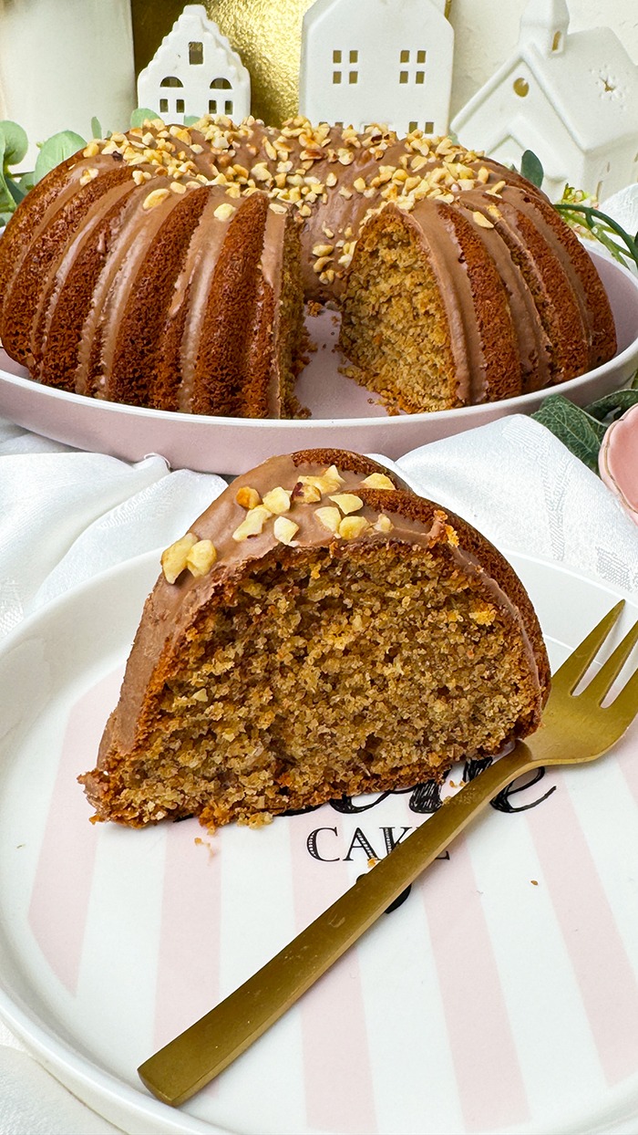 Ein saftiger nusskuchen im gugelhupf-stil mit haselnussglasur und gehackten nüssen liegt auf einem dekorativen teller, während der gesamte kuchen im hintergrund präsentiert wird.