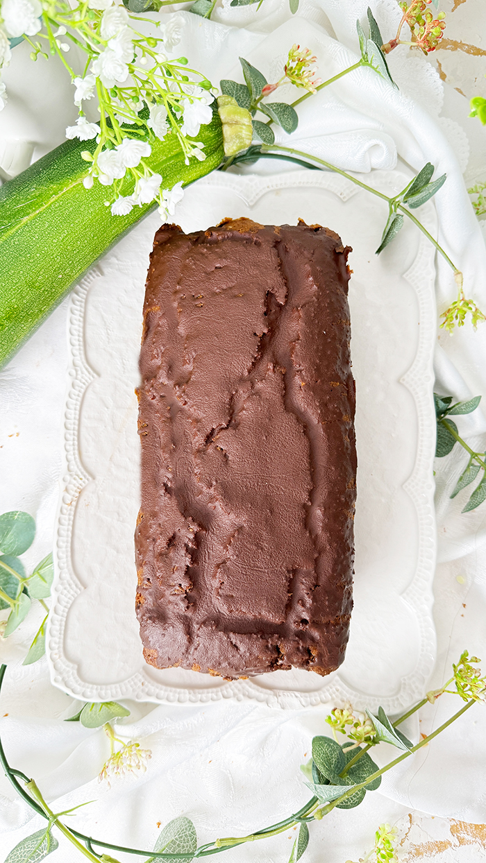 Ein saftiger Zucchinikuchen mit Schokolade, veredelt durch eine glänzende Glasur und Schokostückchen, ideal für gemütliche Kaffeepausen.