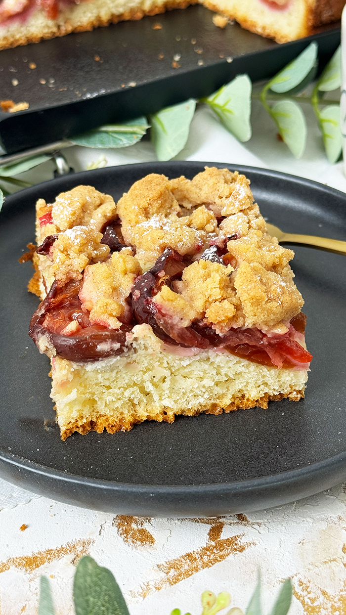 Ein frisch gebackener Zwetschgenkuchen auf einem weißen Teller, bedeckt mit goldbraunen Zimtstreuseln